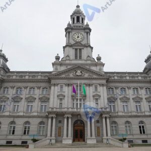 Городская ратуша с часами и флагами перед входом.