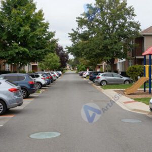 Жилая улочка с припаркованными машинами и детской площадкой.