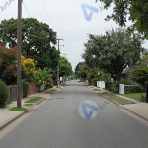 Тихая улочка частного сектора с низкими заборами и садами.