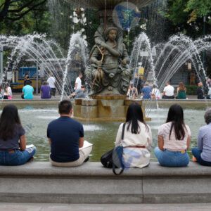 Люди сидят на ступенях у городского фонтана