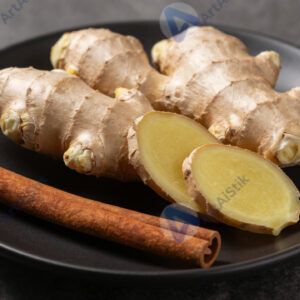 Свежий имбирь и кусочек корицы на чёрной тарелке.