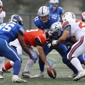 Футболисты в форме разных цветов борются за мяч на мокром поле.