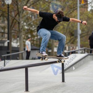 Скейтбордист делает трюк над периллами в городском парке.