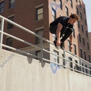 Паркур‑райдер прыгает с перил на стену в городе.