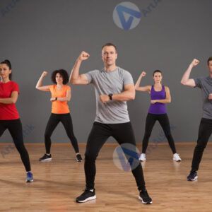 Группа людей в студии выполняет аэробную тренировку.