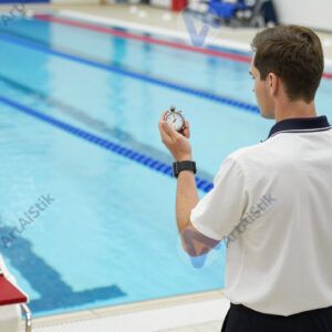 Судья с секундомером стоит у дорожки бассейна.