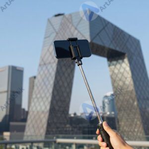 Селфи‑палка со смартфоном на фоне городской достопримечательности.