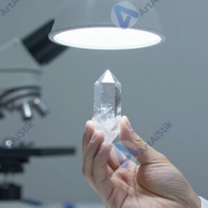Учёный держит в руке прозрачный кристалл под лампой.