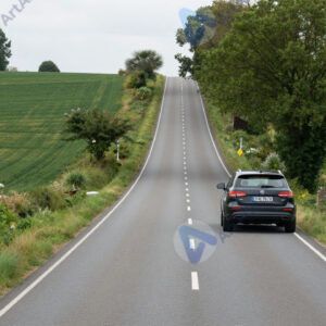 Автомобиль на загородной трассе среди полей и деревьев.