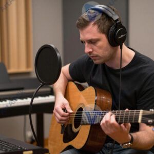 Музыкант в наушниках записывает гитарную партию в студии.