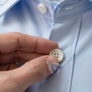 Рука пришивает пуговицу к рубашке крупным планом.