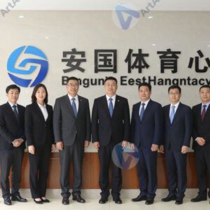 Команда позирует на фоне логотипа компании в холле офиса.